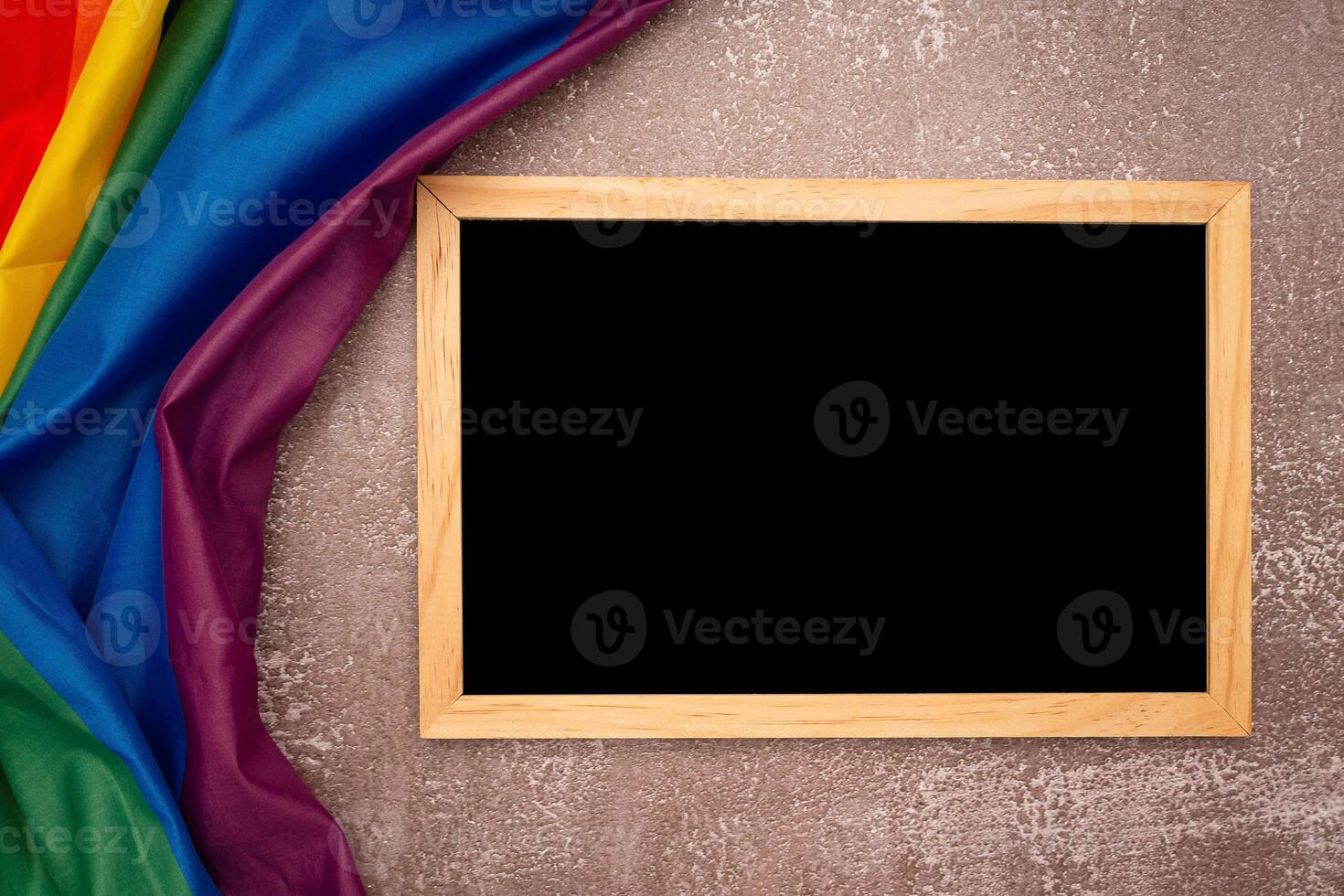 Top view of the rainbow flag or LGBT and a blank mini chalkboard with the wooden border over a cement floor photo