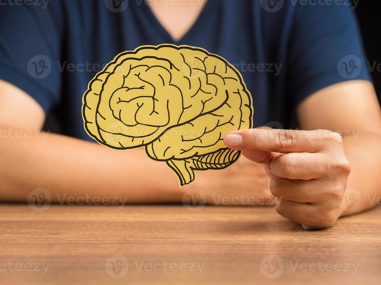 Man in a casual holding a brain shape made from yellow paper while sitting at the table photo