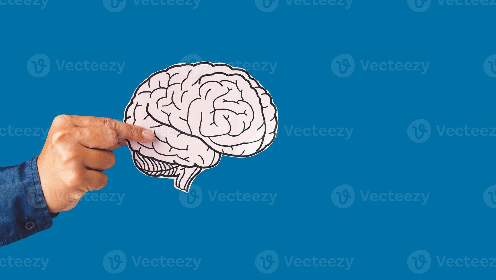 Close-up of hand holding a brain shape made from paper standing against a blue background photo