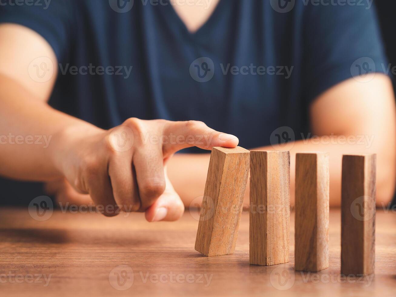 Risk and strategy in business concept. Close-up of hand pushing a wooden block on a line of dominos while sitting in the office photo