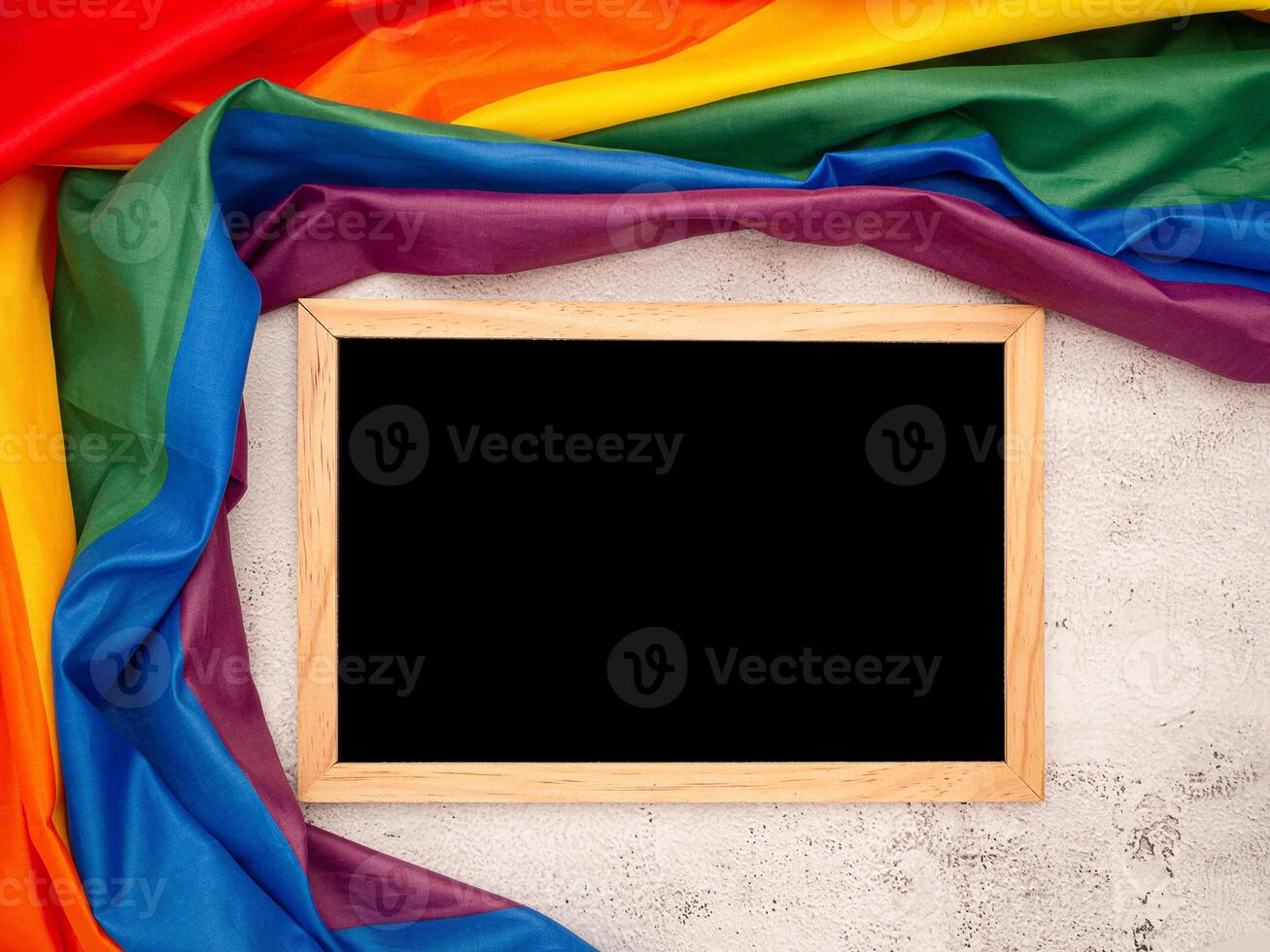 Top view of the rainbow flag or LGBT and a blank mini chalkboard with the wooden border over a cement floor photo