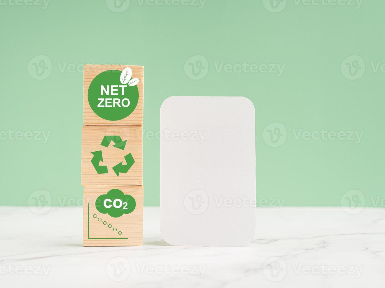 Net-zero greenhouse gas emissions target. Wooden cubes with green icons over a marble floor against a light green background photo