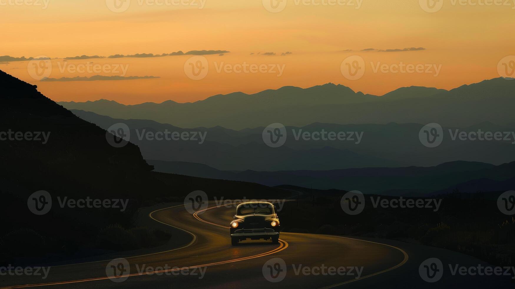 Vintage car silhouette on a winding road with mountains at dusk photo