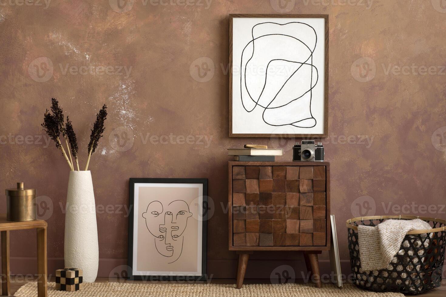 Creative compostion at living room interior with mock up poster frame, design wooden sideboard, brown wall, plaid in basket, camera, beige vase with dried flowers and elegant personal accessories. photo