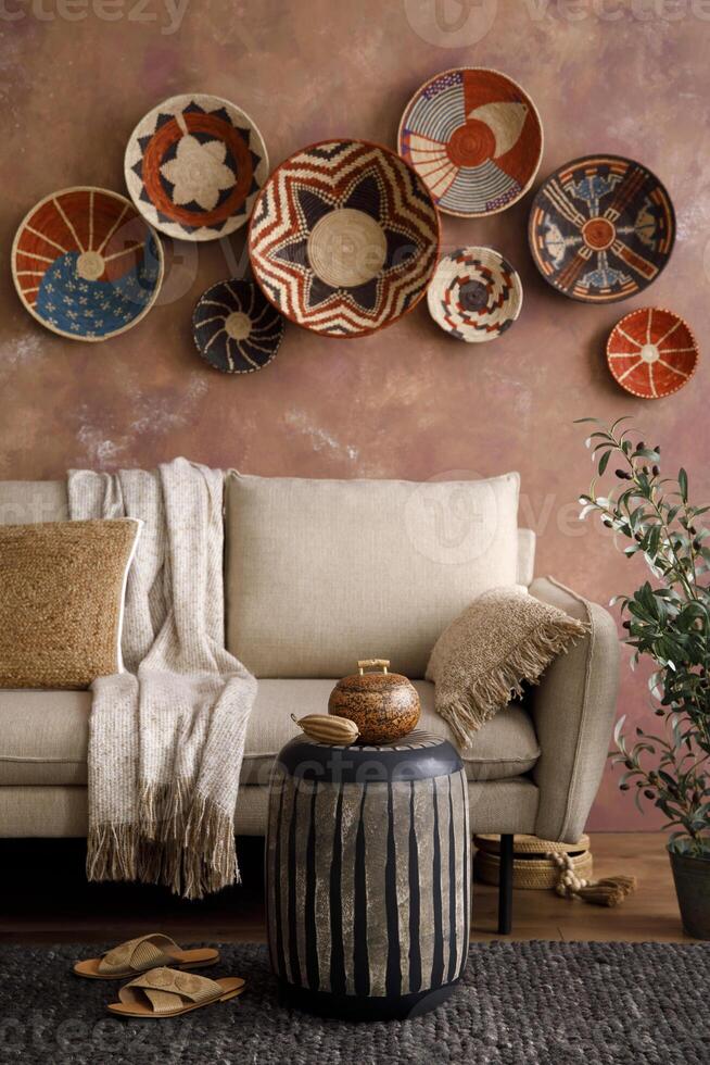 The stylish boho compostion at living room interior with design beige sofa, coffee table, wicker baskets and elegant personal accessories. Brown and white pillows and plaid. Cozy apartment. photo