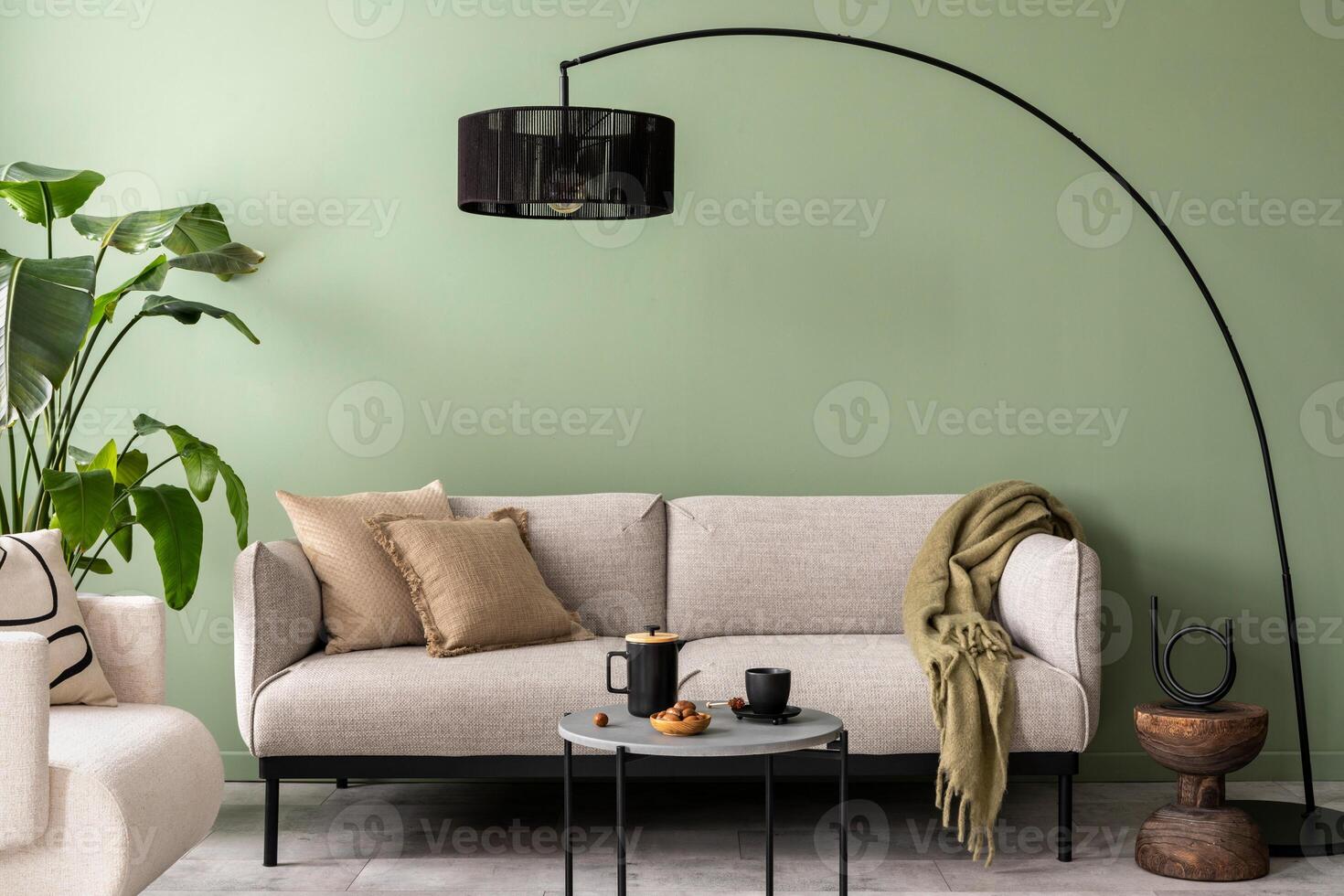 The stylish composition at living room interior with green wall, design gray sofa, coffee table, dark lamp and elegant personal accessories. Beige pillow and plaid. Cozy apartment. Template. photo