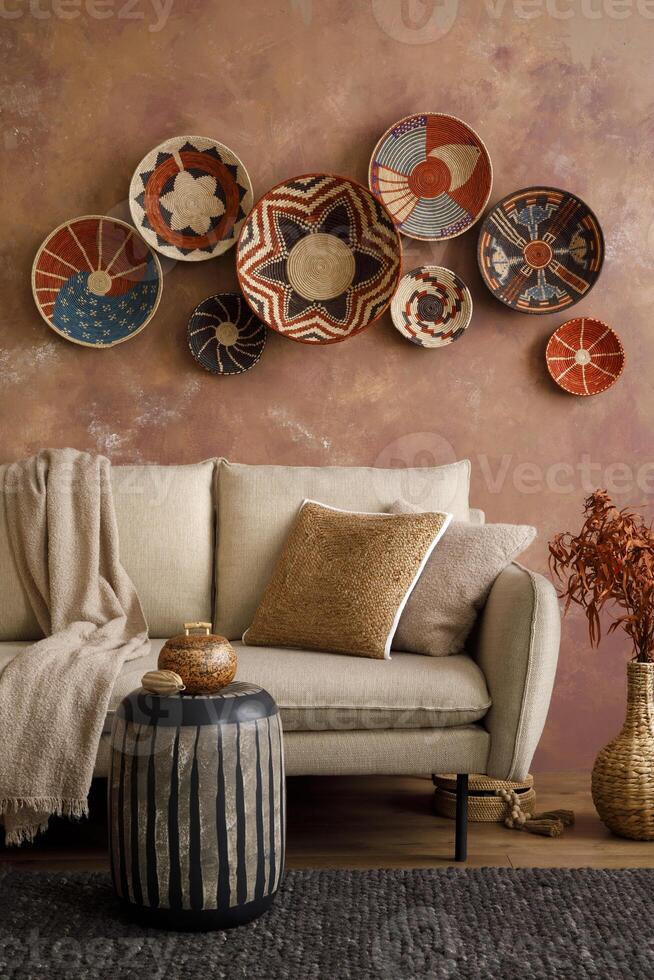 The stylish boho compostion at living room interior with design beige sofa, coffee table, wicker baskets and elegant personal accessories. Brown and white pillows and plaid. Cozy apartment. Home decor photo