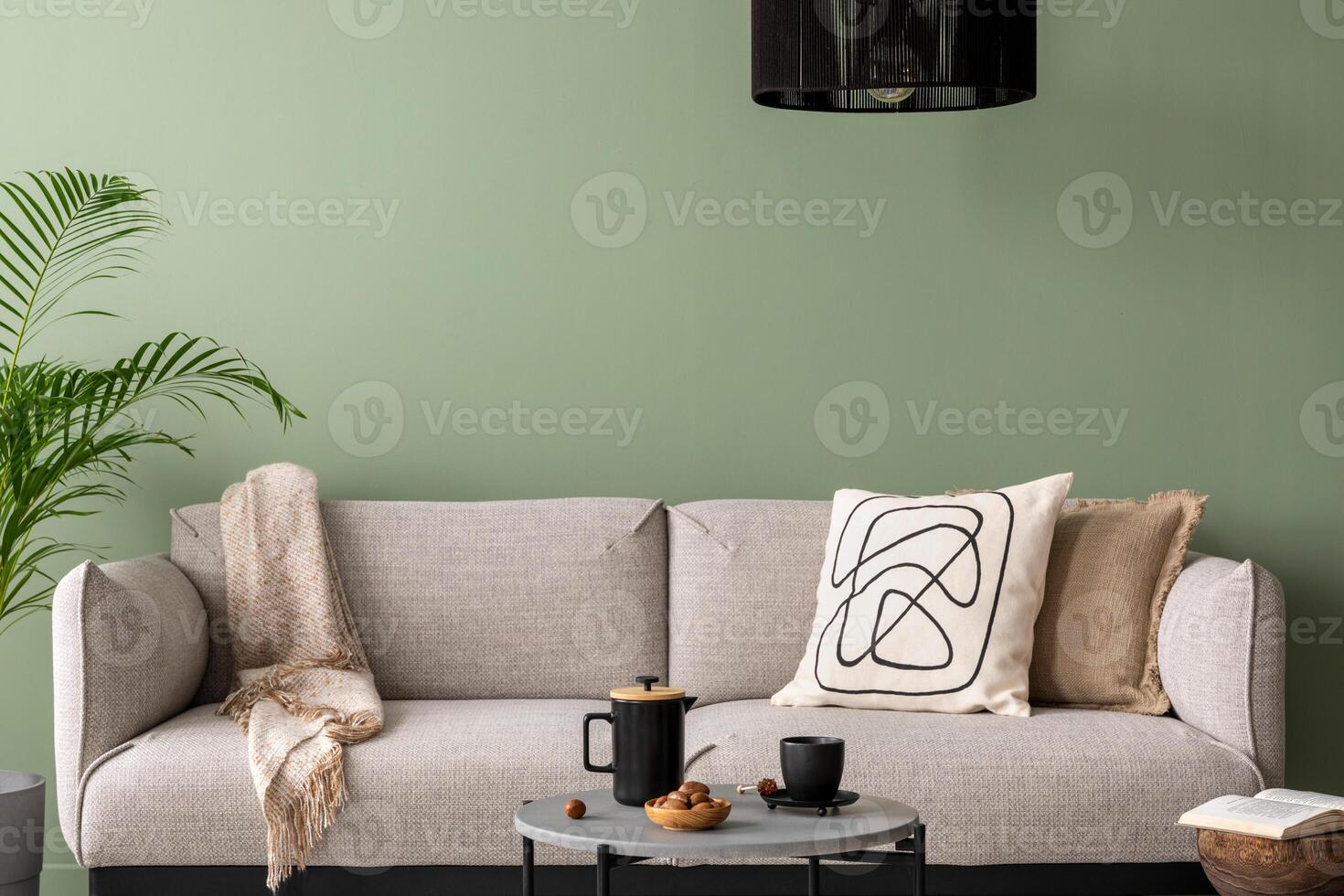 The stylish composition at living room interior with green wall, design gray sofa, coffee table, dark lamp and elegant personal accessories. Beige pillow and plaid. Cozy apartment. Template. photo