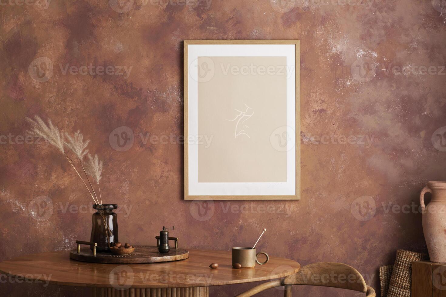 Stylish boho vintage dining room interior with poster mock up. Round table with wooden tray, vase with dried flowers and cup. Brown wall and rattan lamp. Mock up poster. Template. photo