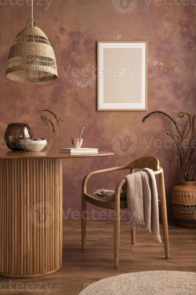 Stylish boho vintage dining room interior with poster mock up. Round table with rattan chair, vase with dried flowers. Brown wall and rattan lamp. Mock up poster. Template. photo