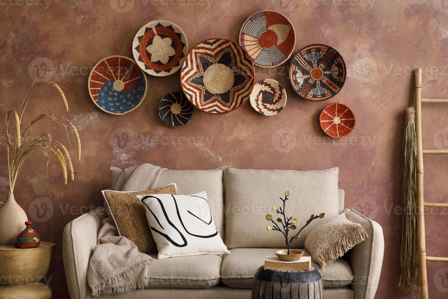 The stylish boho compostion at living room interior with design beige sofa, coffee table, stool wicker baskets and personal accessories. Brown and white pillows and plaid. Cozy apartment. Template. photo