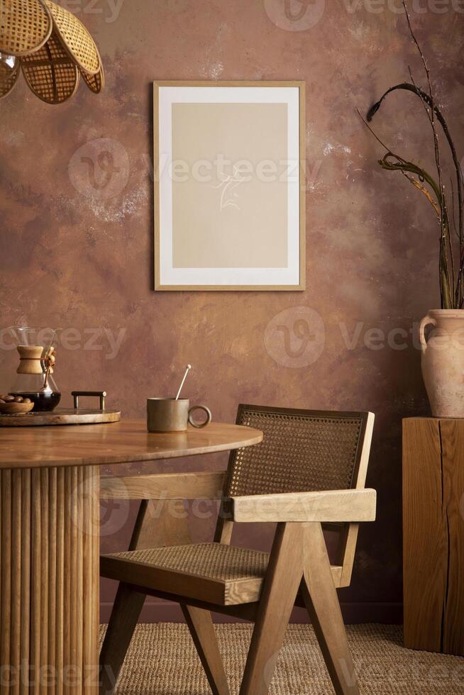 Stylish boho vintage dining room interior with poster mock up. Round table with rattan chair, vase with dried flowers. Brown wall and rattan lamp. Mock up poster. Template. photo