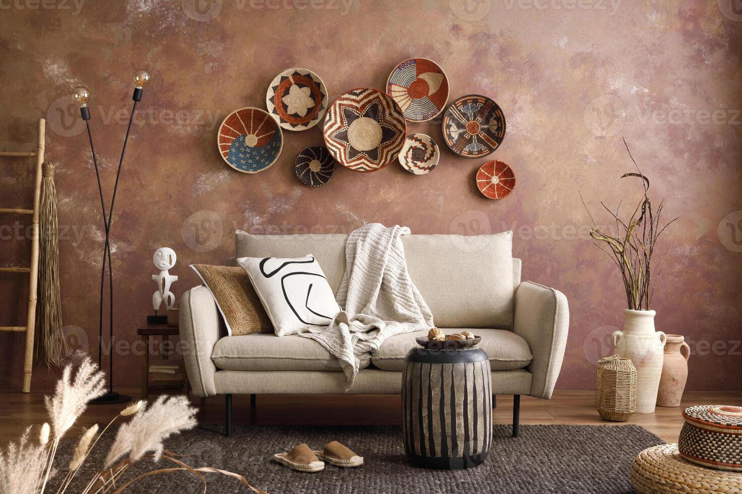 The stylish boho compostion at living room interior with design beige sofa, coffee table, wicker baskets and elegant personal accessories. Brown and white pillows and plaid. Cozy apartment Home decor photo