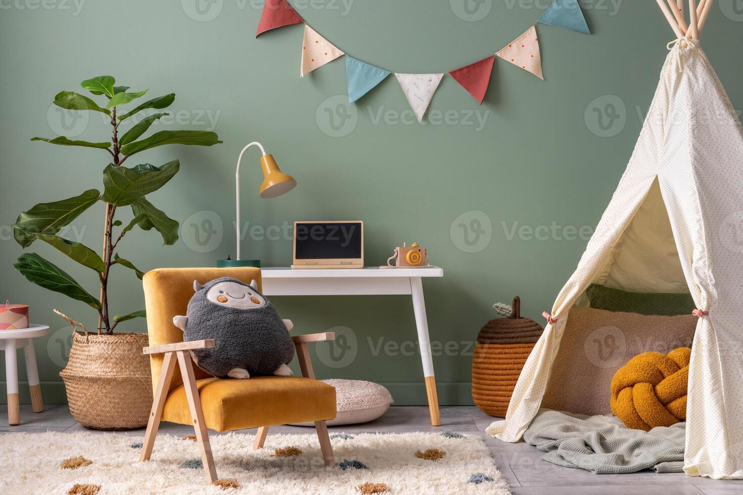 Creative composition of stylish and cozy child room interior design with green wall, plush toys, plant in basket, lamp, bright carpet, hut, desk, armchair, stool and lamp. Panels floor. Template. photo
