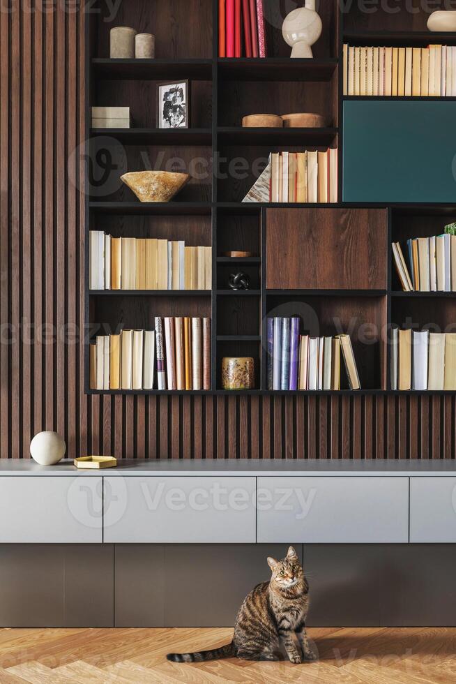 Modern bookcase in lamells wall. Grey chest of drawers. Bookcase a lot of books and accessories. Herringbone wooden parquet. Cat in open spaces. photo