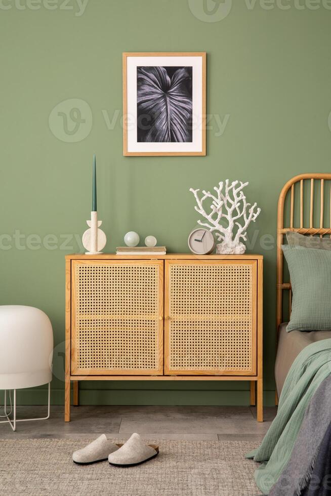 Stylish composition of modern bedroom interior. Mock up poster frame, rattan commode, beautiful bedclothes and creative personal accessories. Sgae green wall. Template. Copy space. photo