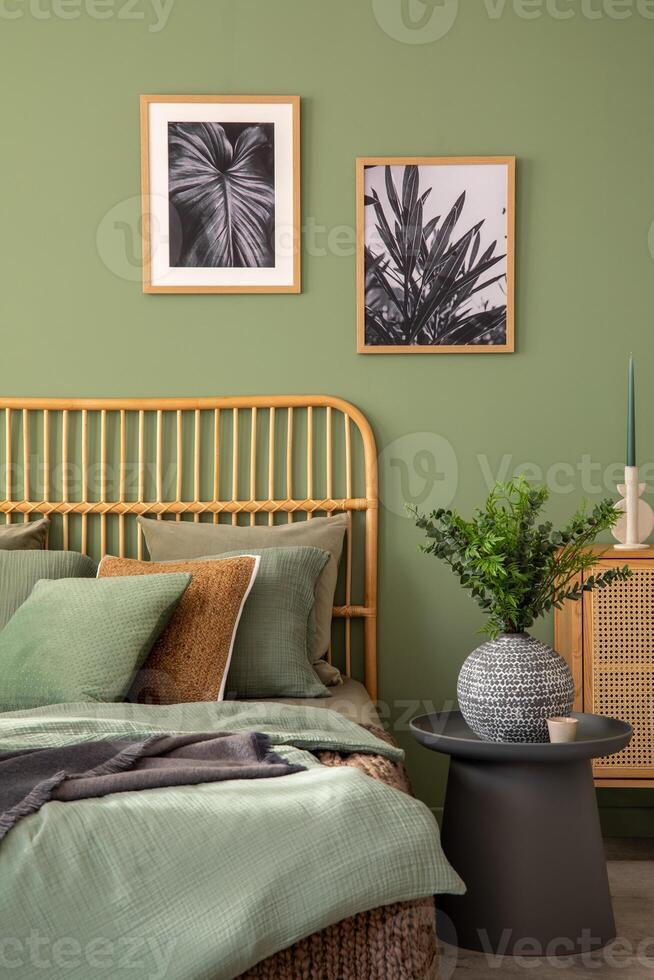 Stylish bedroom interior design with mock up poster frames, bed, side table, rattan commode, vanity table and creative home accessories. Sage green wall. Template photo