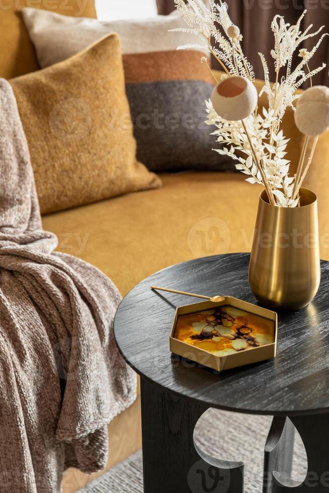 Stylish composition of modern living room. Stylish coffe table with tray and gold vase with dried flowers. Yellow sofa with plaid and pillows. Template. photo