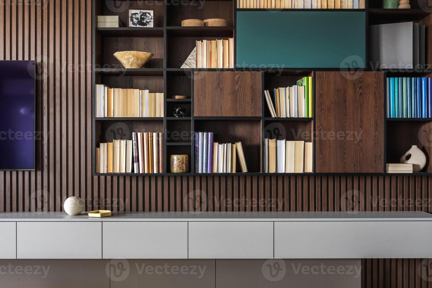 Modern bookcase in lamells wall. Grey chest of drawers. Bookcase a lot of books and accessories. Herringbone wooden parquet. Cat in open spaces. photo