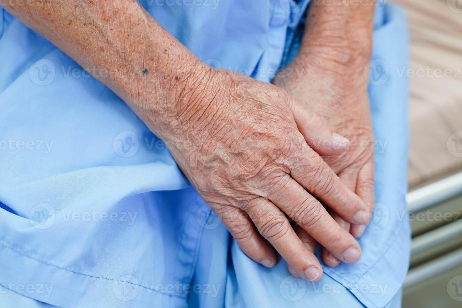 Asian elder senior woman patient sitting on bed in hospital, closeup at her hand. photo