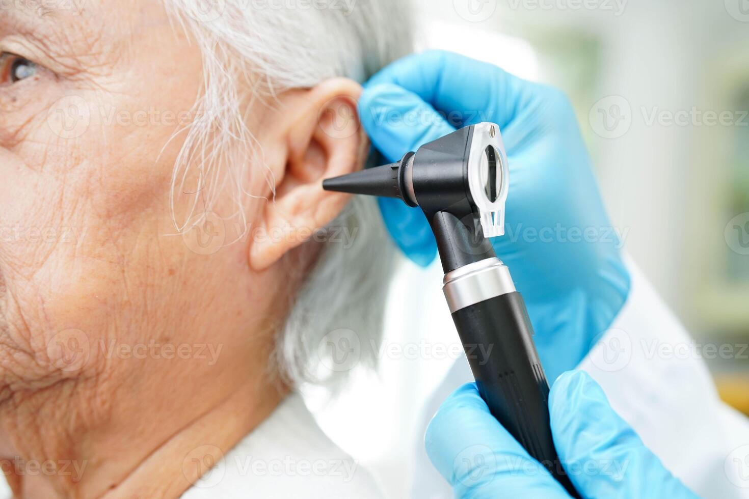 Otolaryngologist or ENT physician doctor examining senior patient ear with otoscope, hearing loss problem. photo