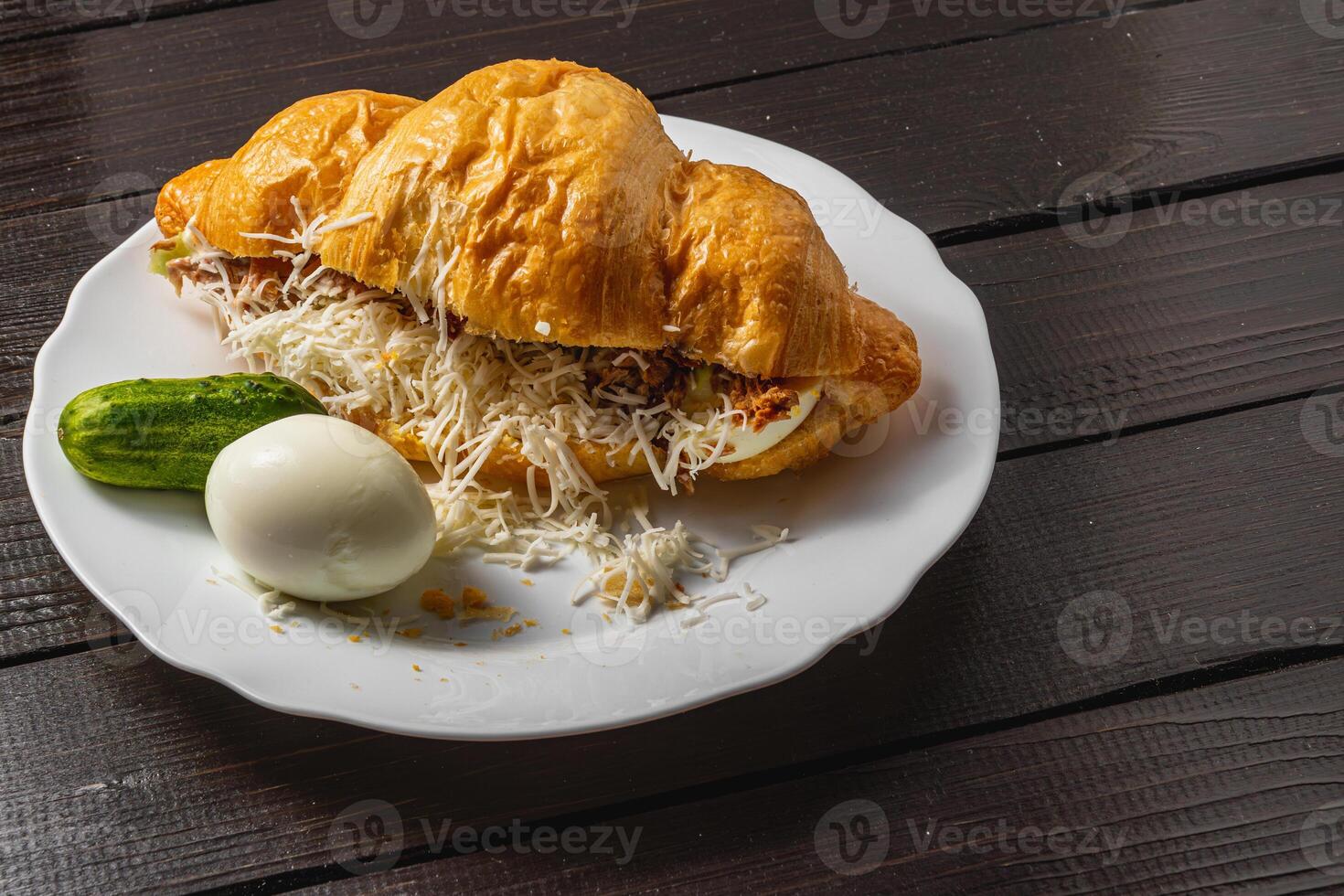 Croissant sandwich with tuna, egg, cucumber and cheese on a white plate photo