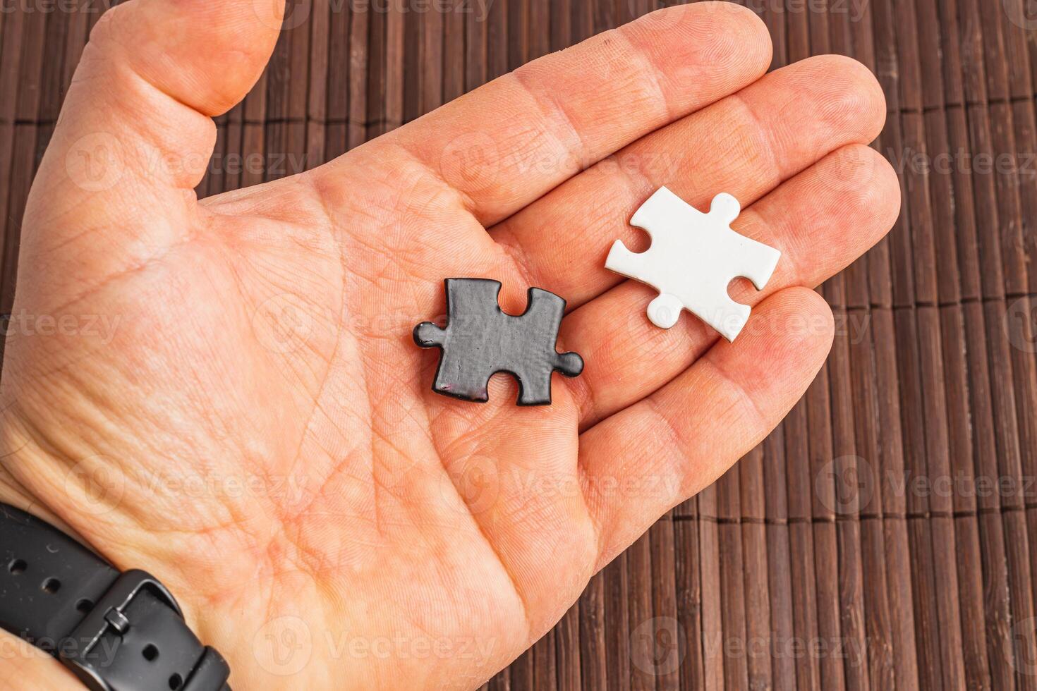 A hand holding two puzzle pieces one white and one black, difficult choice photo