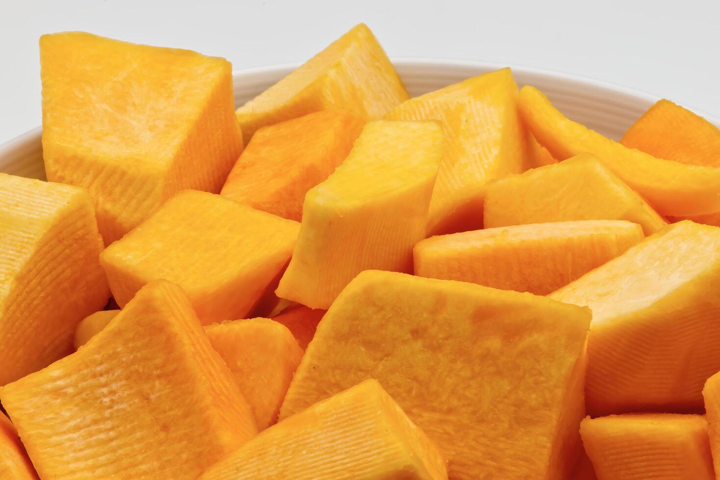 A close-up view of diced pumpkin pieces in a white bowl. photo
