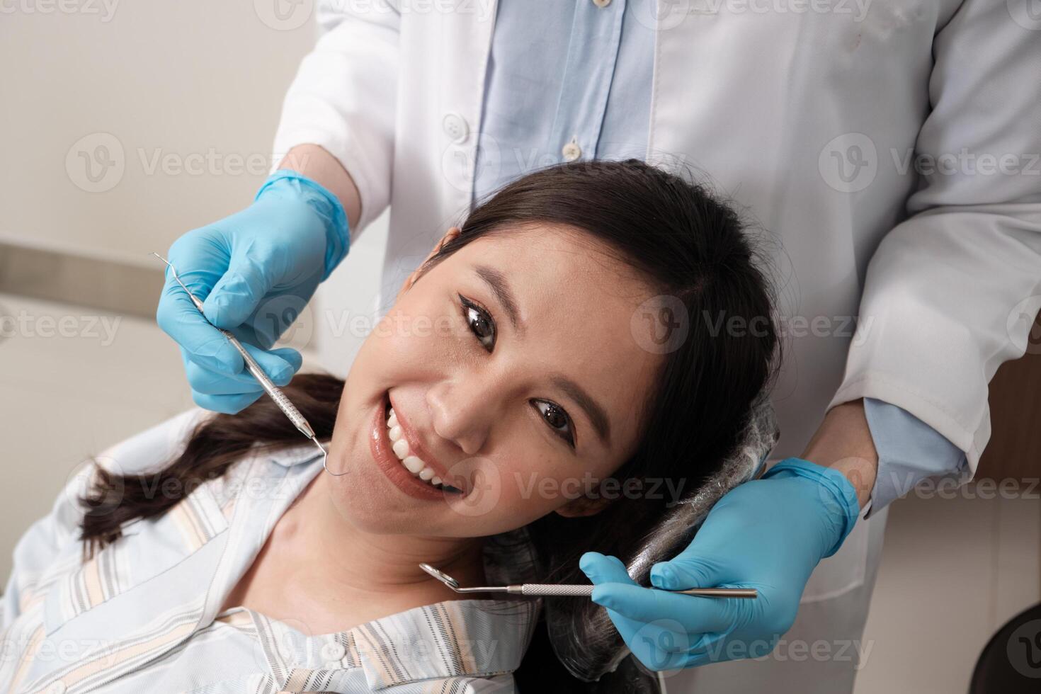 Close-up shot of beautiful Asian female face, white teeth, and cheerful face in dentist's hand, dental treatment with tooth whitening and cleaning in doctor hospital clinic, oral hygiene healthcare. photo