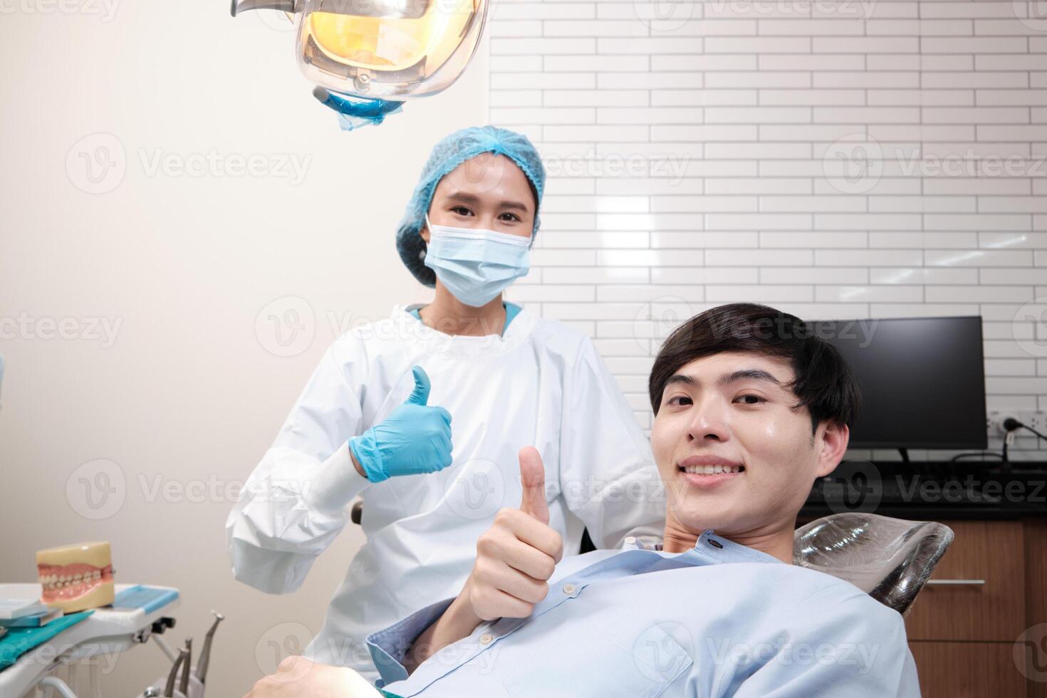 Portrait of Asian female dentist and male patient thumbs up, tooth whitening implant, happy smile, and looking at camera in dental clinic, mouth hygiene healthcare work in a doctor's hospital. photo