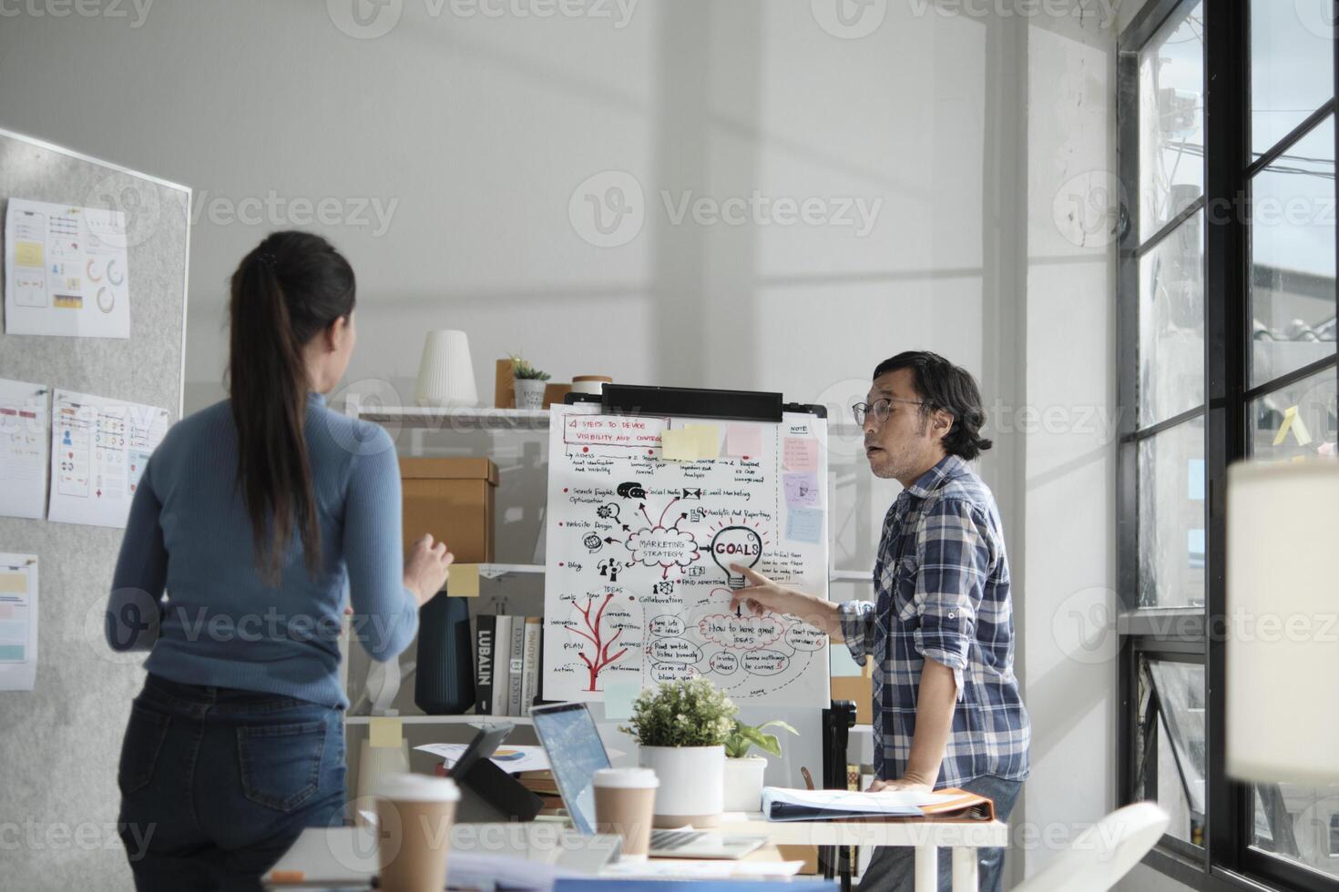 Two young Asian startup company partners discuss and brainstorm in casual small business office, marketing planning ideas, and creatively freelance work as E-commerce entrepreneur and coworker team. photo
