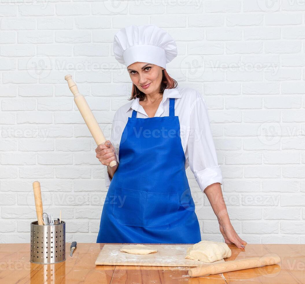 portrait of mature woman in cook uniform with rolling pin and dough photo