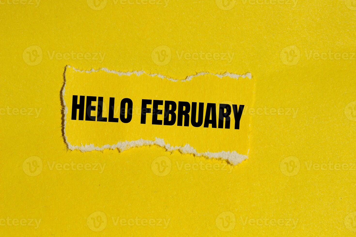 Hello february message written on ripped yellow torn paper piece with yellow background. Conceptual hello february symbol. Copy space. photo