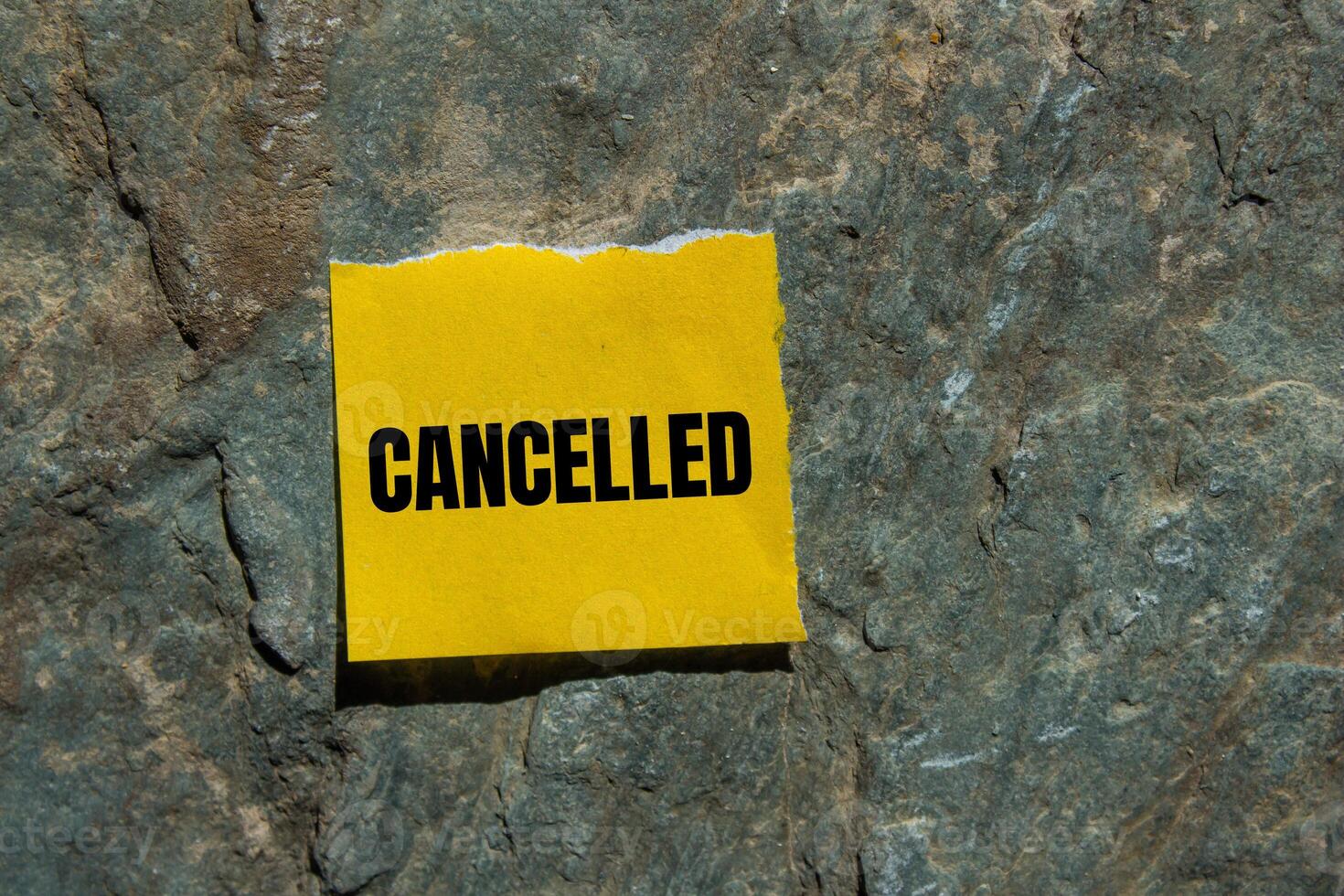 Cancelled message written on ripped torn yellow paper piece with stone background. Conceptual cancelled symbol. Copy space. photo