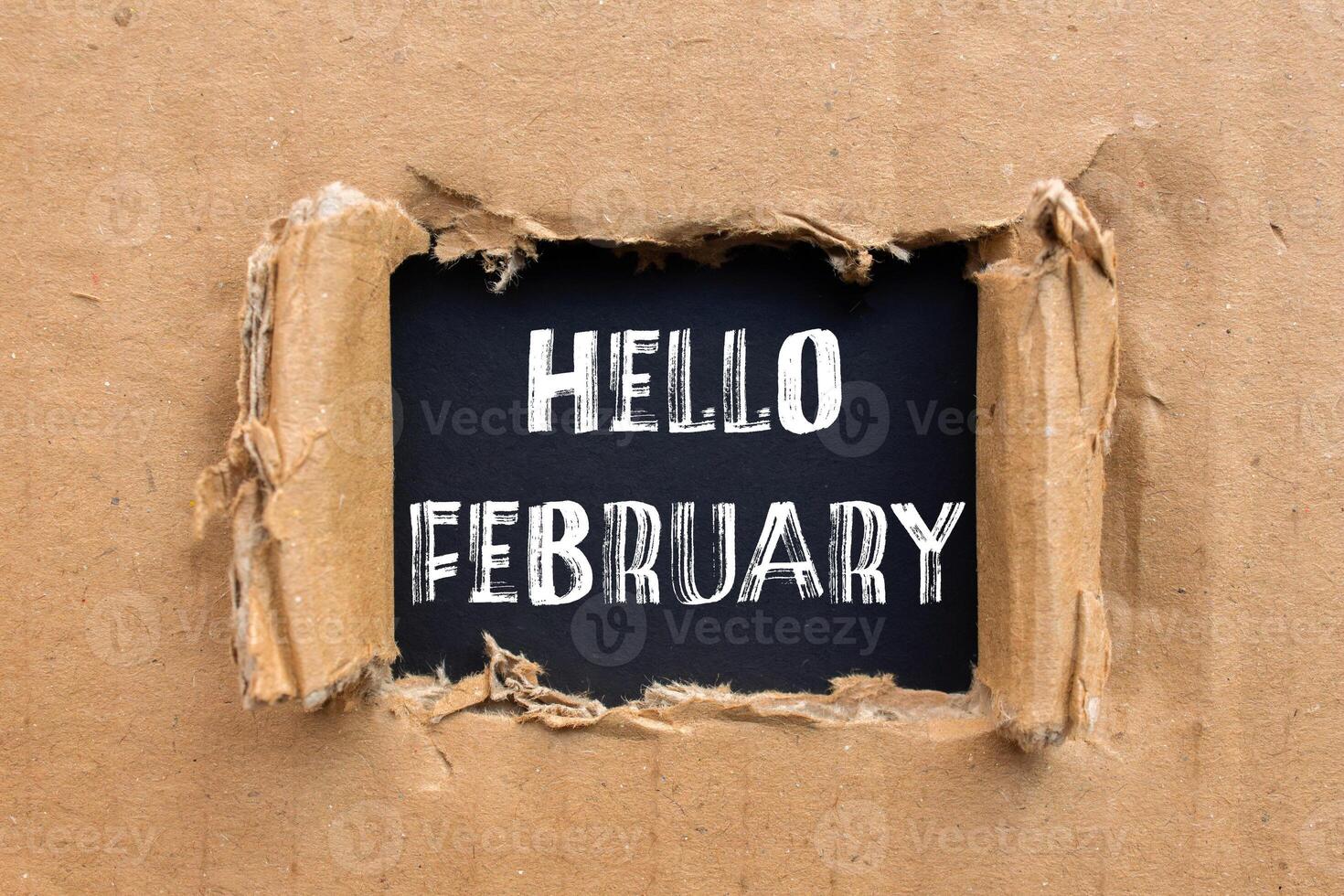 Hello february message written on ripped torn cardboard paper with black background. Conceptual hello february symbol. Copy space. photo