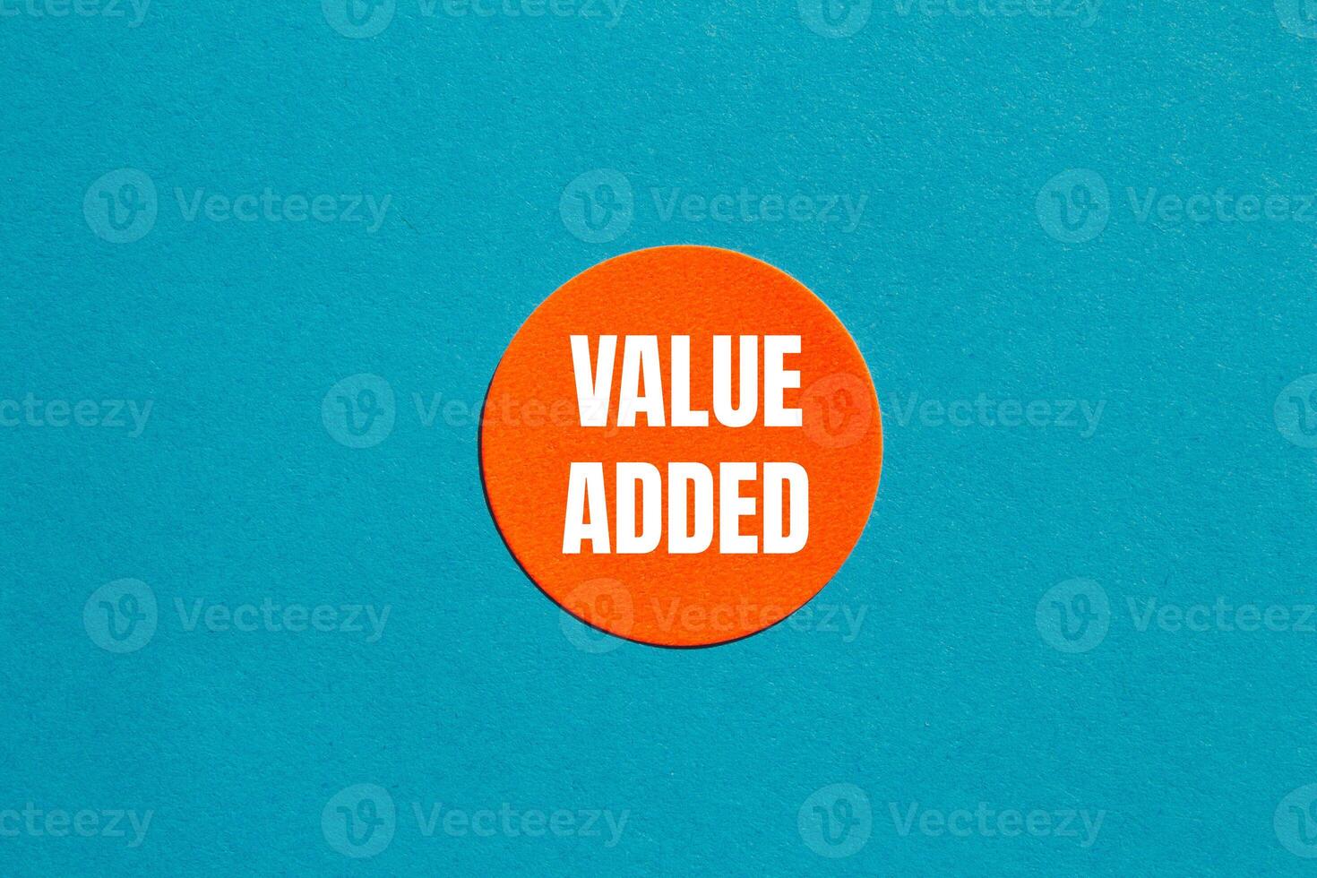 Value added message written on round orange sticker with blue background. Conceptual value added symbol. Copy space. photo