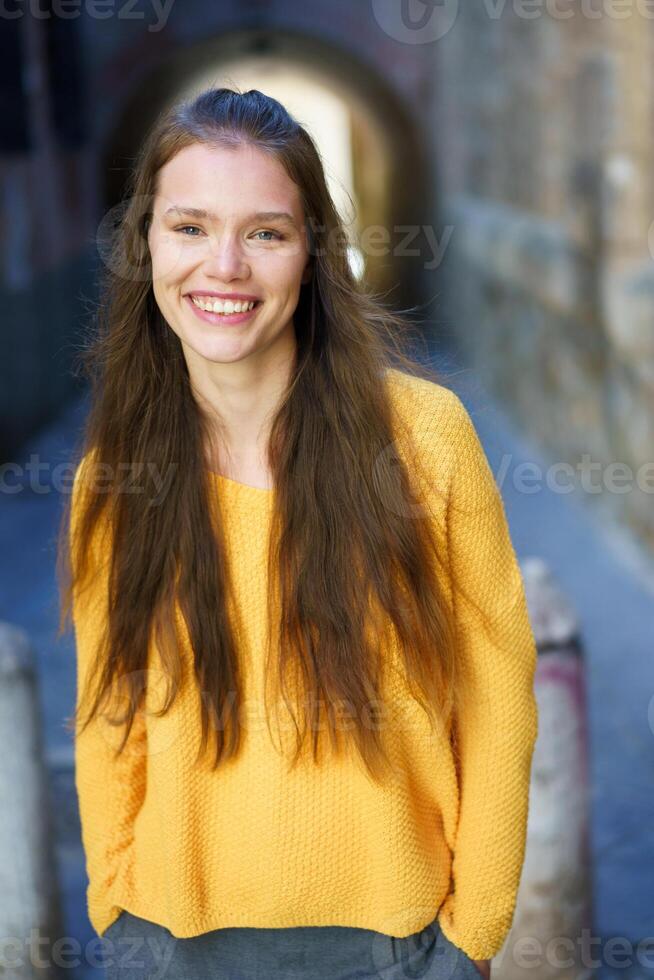 A cheerful woman in a yellow sweater posed in an urban setting with vibrant city colors photo