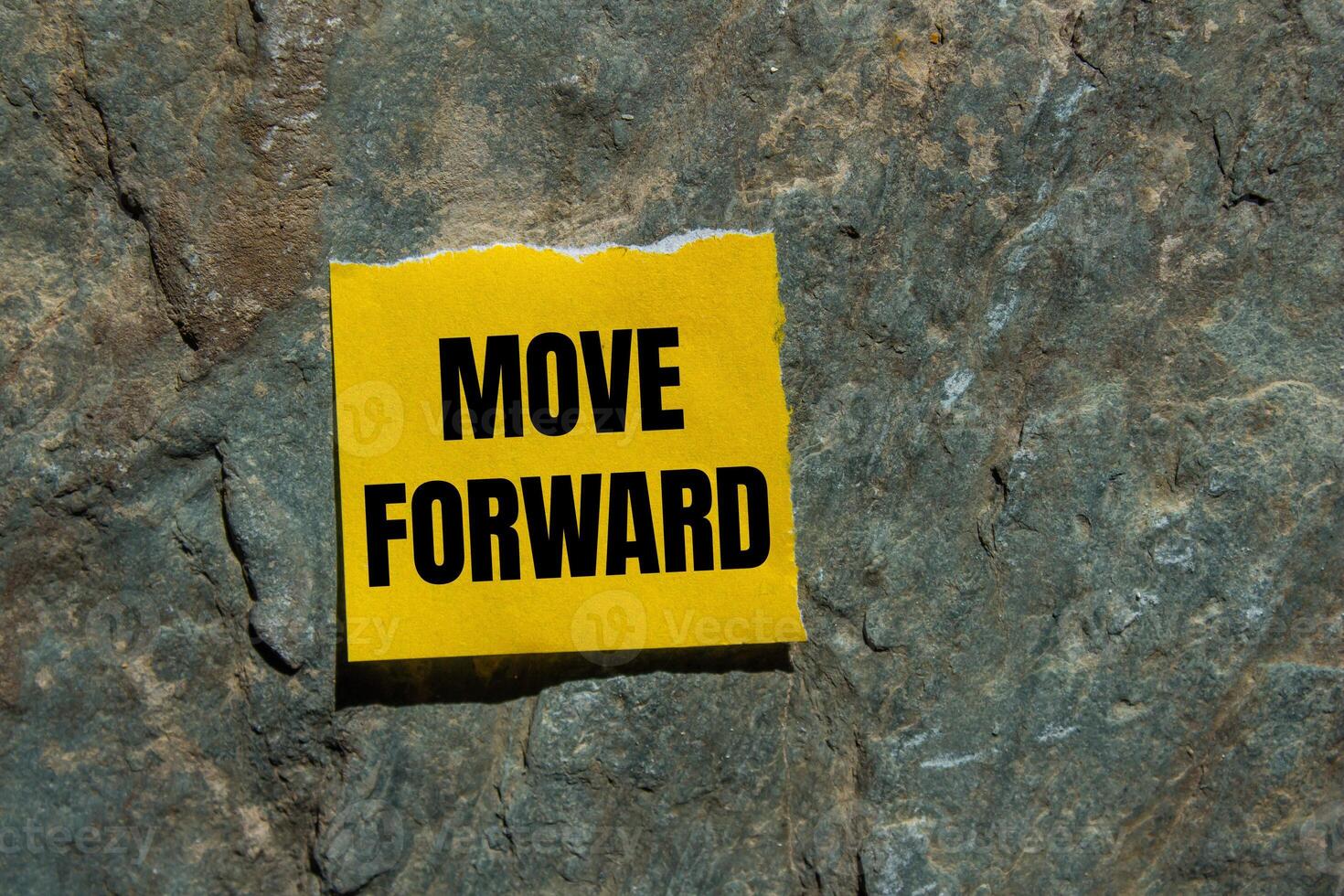 Move forward message written on ripped torn yellow paper piece with stone background. Conceptual move forward symbol. Copy space. photo