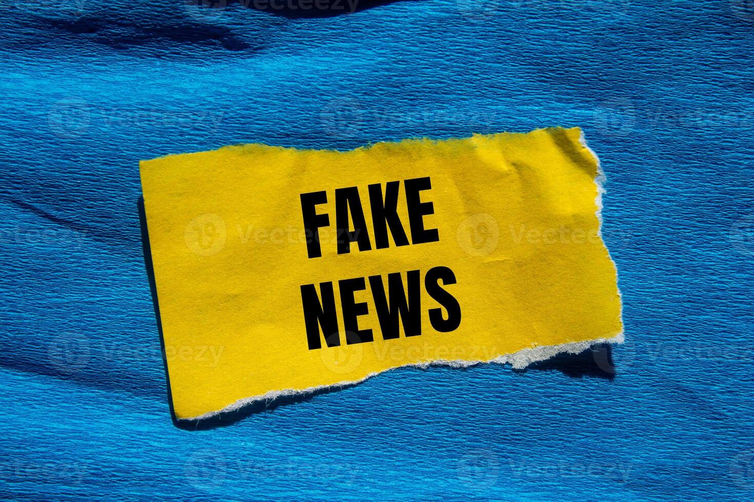 Fake news message written on ripped torn yellow paper piece with blue background. Conceptual fake news symbol. Copy space. photo
