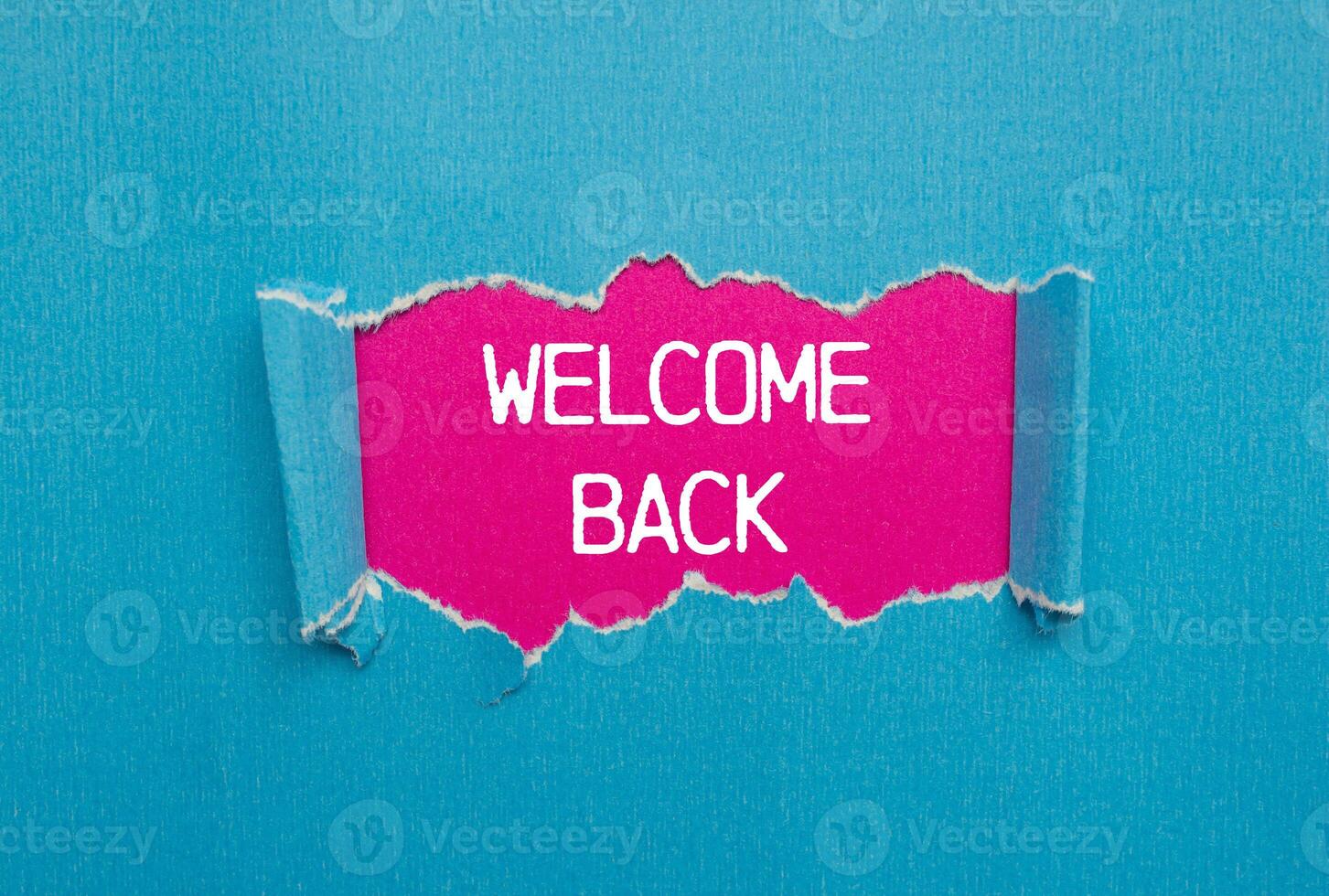 Welcome back message written on ripped torn blue paper with pink background. Conceptual welcome back symbol. Copy space. photo