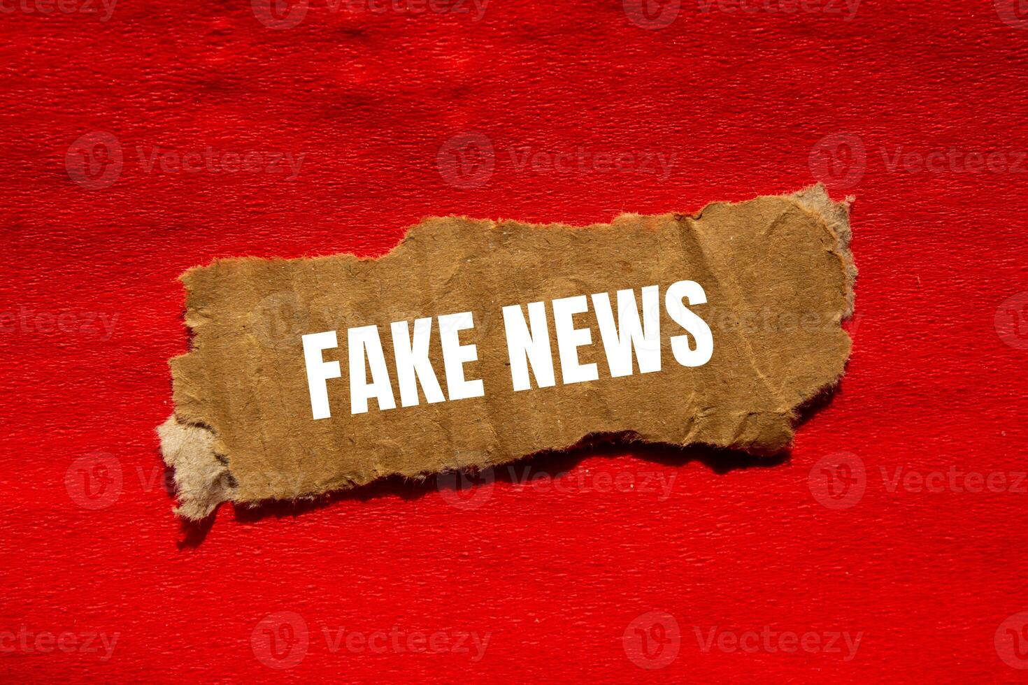 Fake news message written on ripped torn cardbaord paper piece with red background. Conceptual fake news symbol. Copy space. photo