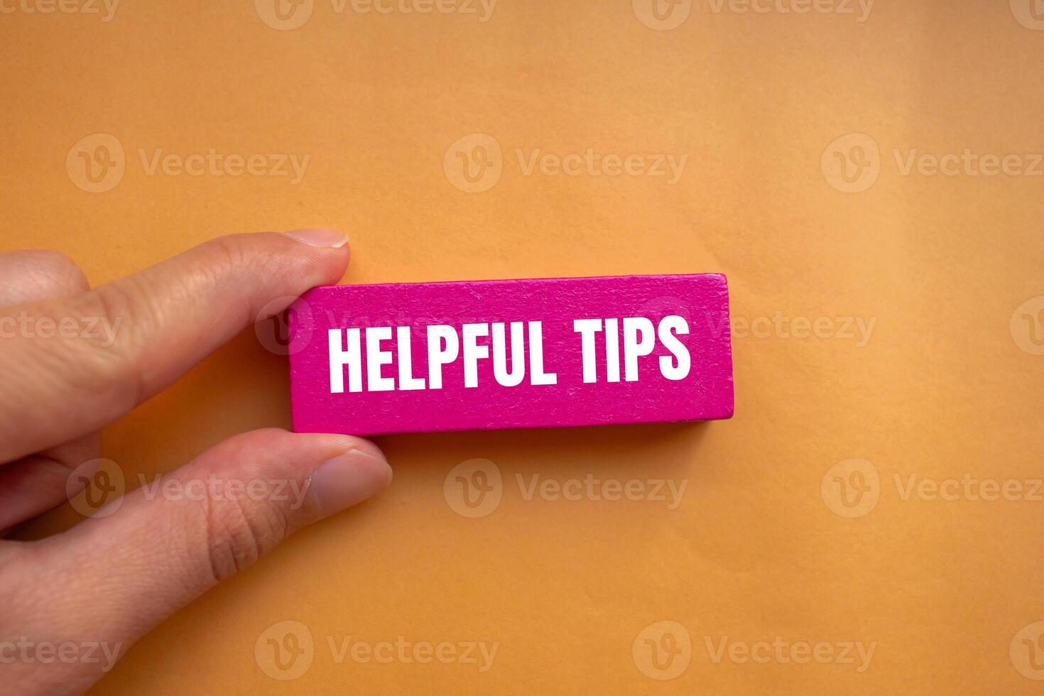 Helpful tips message written on pink wooden block with orange background. Conceptual helpful tips symbol. Copy space. photo