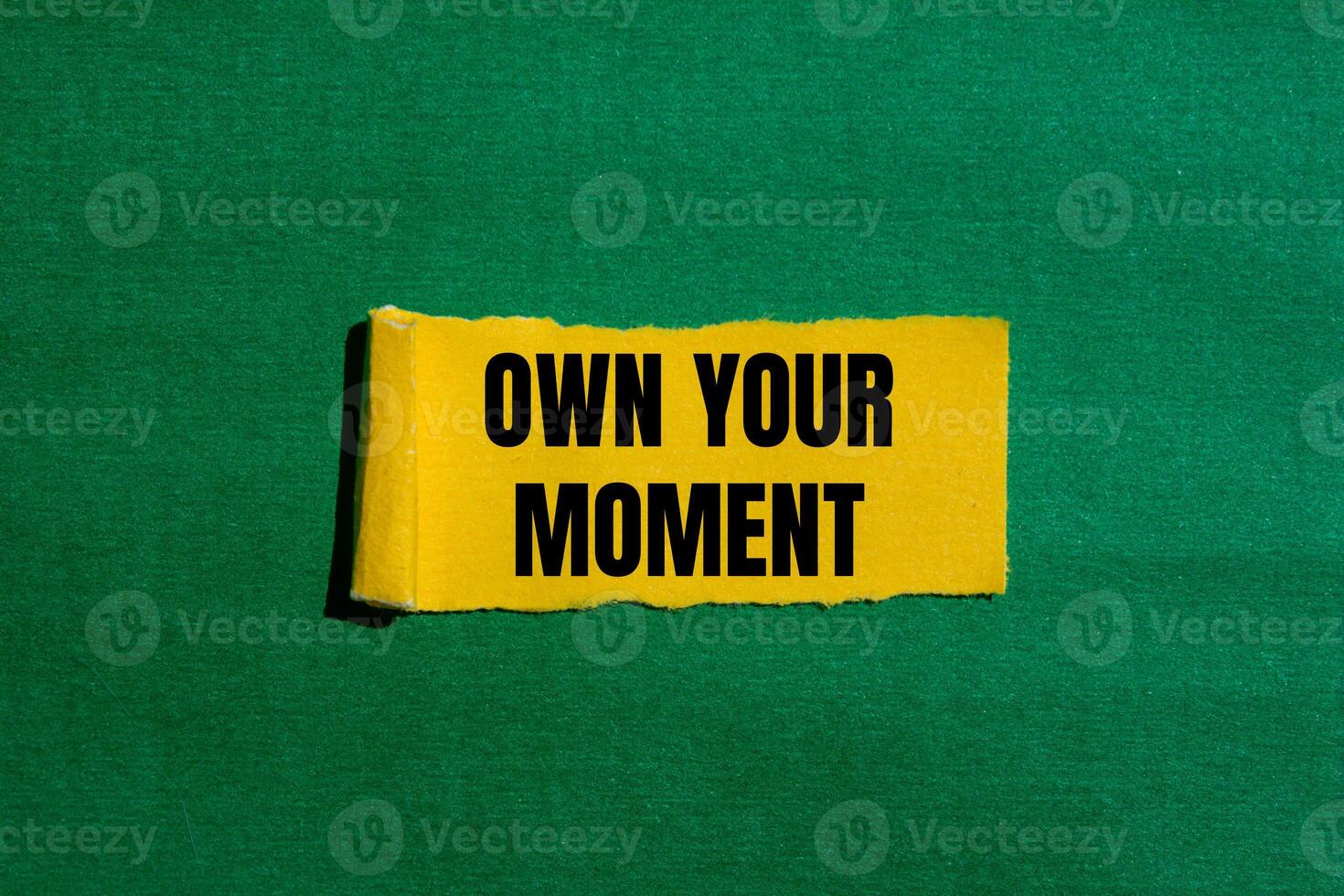 Own your moment message written on ripped torn yellow paper piece with green background. Conceptual own your moment symbol. Copy space. photo