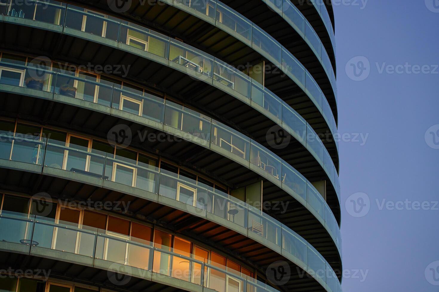 Modern round residential building with balconies at sunset. Contemporary architecture with curved design. Minimalistic style of apartment building with glass facade photo