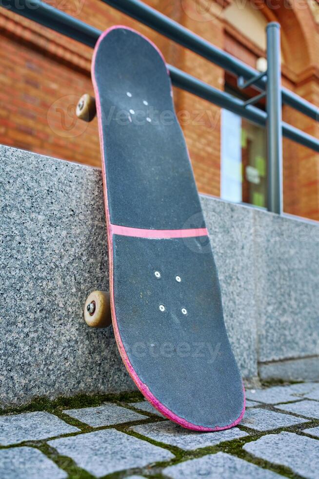 Used scratched pink skateboard against stone wall at city street. Urban sport and youth subculture concept photo