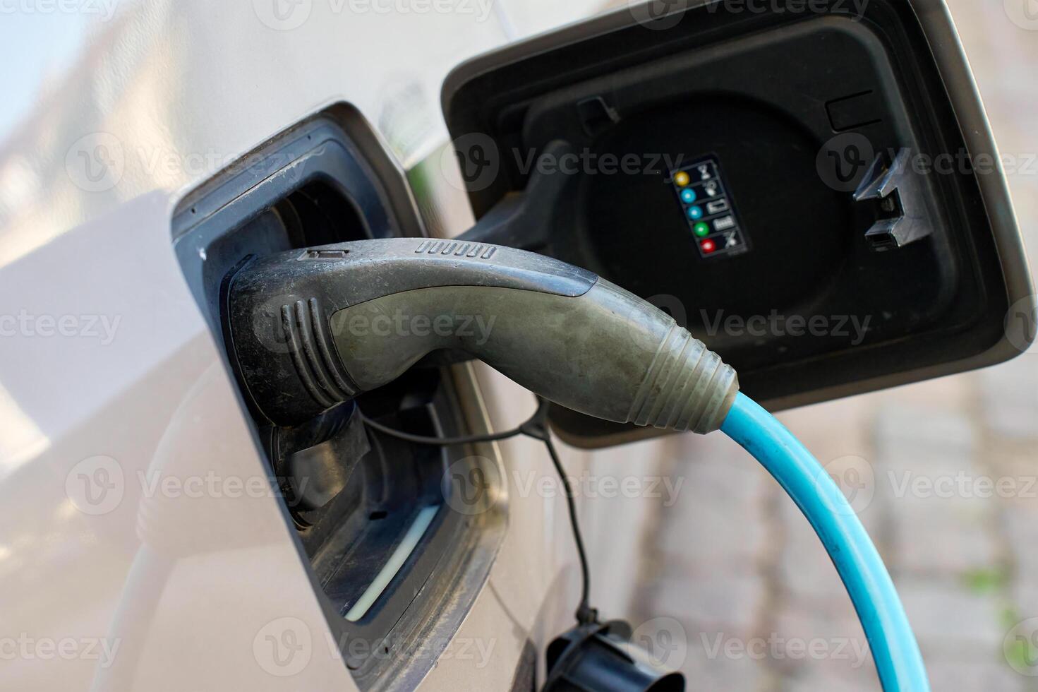 Close up of electric vehicle charging on public station at city street. EV car with plugged in cable recharging battery. Sustainable and eco-friendly transportation photo
