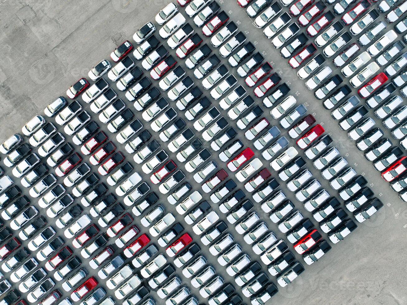 Aerial view of new cars stock at factory parking lot. Above view cars parked in a row. Automotive industry. Logistics business. Import or export new cars at warehouse. Big parking lot at port terminal photo