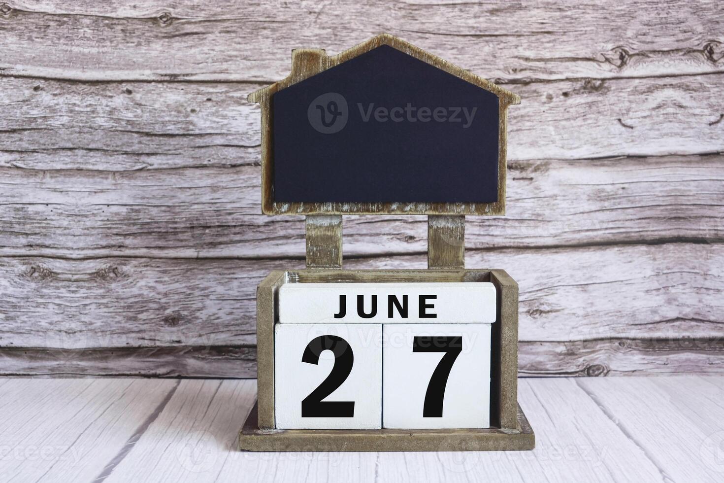 Chalkboard with June 27 date on white cube block on wooden table. photo