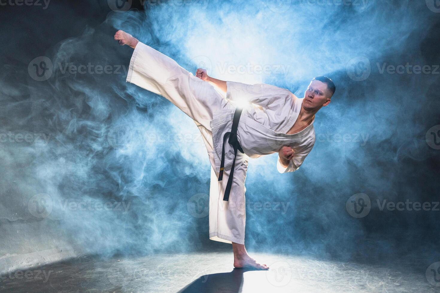 Strong man fighter in white kimono for karate martial arts with black belt preparing for fight training in black background. Man training moves kicks practicing shadow fight ready for sparring photo
