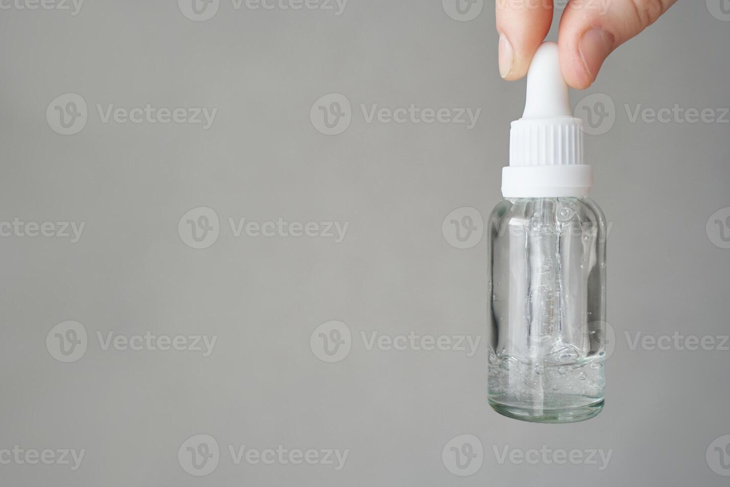 Hand holding clear dropper bottle with liquid against gray background for skincare or essential oils use. photo